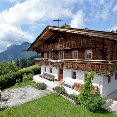 A traditional chalet in the Alps with wooden cladding and a beautiful view of the mountains. The garden is well-kept and offers a cozy outdoor area.