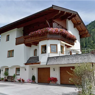A beautiful, modern house with a balcony and colorful flowers. In the background, green mountains can be seen.