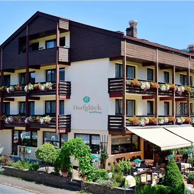 A cozy hotel building with balconies and colorful flowers. It is situated in a green environment and offers an inviting impression.