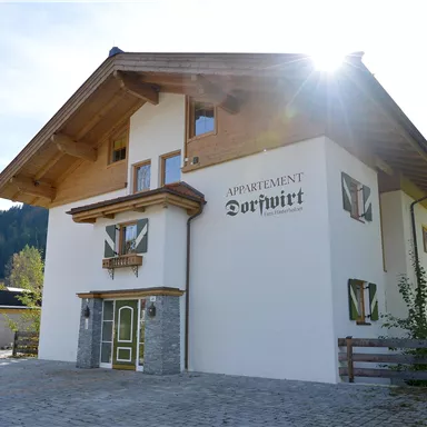 Ein modernes Appartementhaus mit traditioneller Architektur in einer malerischen Landschaft. Die Sonne strahlt auf die Fassade, umgeben von sanften Hügeln.