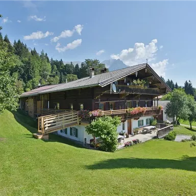 A beautiful wooden house surrounded by green meadows and trees. The sky is clear and sunny, with a few clouds.