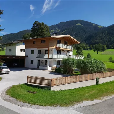 A beautiful house in the mountains with a well-maintained garden. In the background, green meadows and trees can be seen.