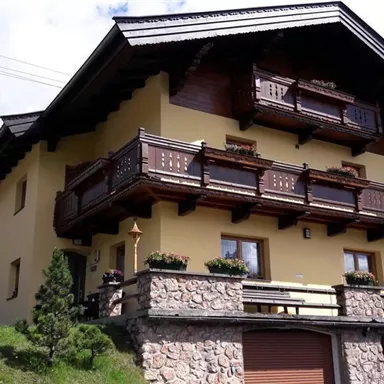 Ein gemütliches Haus im Chalet-Stil mit Holzbalustraden und einem gepflegten Garten. Die Fassade ist in warmen Gelbtönen gehalten und strahlt eine einladende Atmosphäre aus.