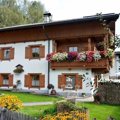 Ein schönes, traditionelles Haus mit Blumenbalkonen und gepflegtem Garten. Das Gebäude hat eine rustikale Holzverkleidung und liegt in einer ruhigen Umgebung.