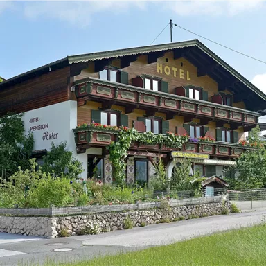Ein traditionelles, zwei- bis dreistöckiges Hotel mit Holzfassade und Balkonen. Es befindet sich umgeben von einer grünen Landschaft und ist mit Pflanzen dekoriert.