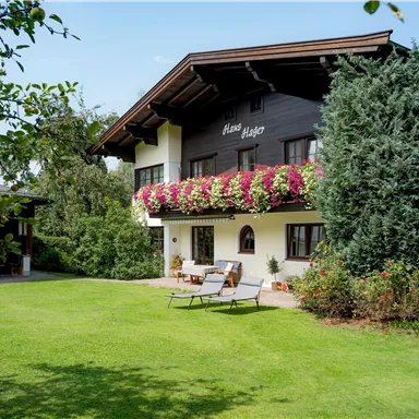 A picturesque house with a balcony, surrounded by lush greenery. The garden offers a relaxing view and cozy loungers.