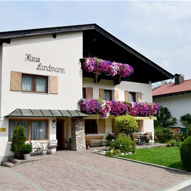 Ein charmantes Haus mit bunten Blumen an den Balkonen. Es hat einen gepflegten Garten und eine einladende Fassade.