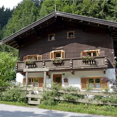 Ein traditionelles Holzhaus mit einem Balkon und Fensterläden. Umgeben von grünen Bäumen und einer ruhigen Landschaft.