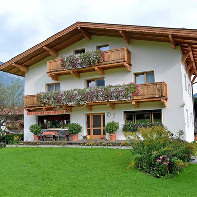 Ein charmantes Haus mit Holzveranda und Blumenkästen. Der gepflegte Garten ist umgeben von Bergen und grünen Bäumen.