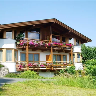 A charming house with a wooden balcony adorned with colorful flowers. Surrounded by green meadows and trees, it exudes an inviting atmosphere.