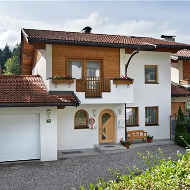 Ein modernes Einfamilienhaus mit einem braunen Satteldach. Vor dem Haus befindet sich ein gepflasterter Weg und ein kleiner Garten.