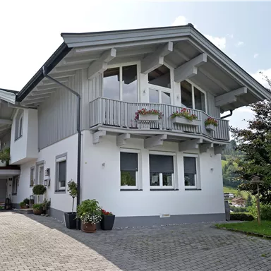 Ein modernes, zweigeschossiges Haus mit einem Balkon und großen Fenstern. Es hat einen schönen Garten und eine gepflasterte Einfahrt.