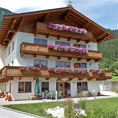 A charming building in alpine style with flower balconies. Surrounded by green mountains and an inviting garden landscape.
