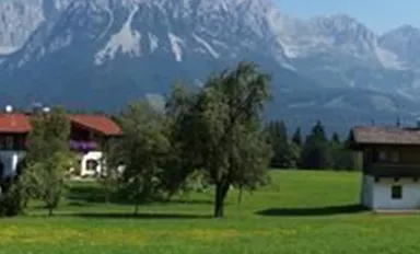 A picturesque landscape with traditional Bavarian houses and lush meadows. In the background, majestic mountains rise under a clear sky.