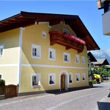 Ein charmantes, gelbes Haus mit einem Balkon und Blumen. Die Straße ist ruhig und von typischer Architektur umgeben.