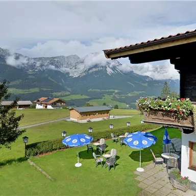 A picturesque Alpine landscape with a cozy inn. In the foreground are blue and white sun umbrellas, and the mountains are surrounded by clouds.