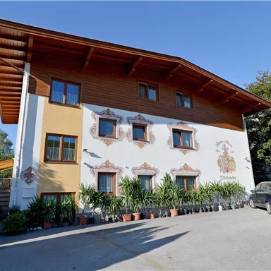 A charming two-story building with a painted facade. In front of the house are many plants and a parked car.