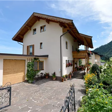 A beautiful house in the mountains with a well-tended garden and an inviting driveway. The sky is clear and there is a peaceful atmosphere.