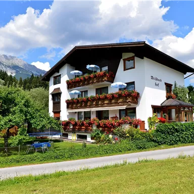 A charming building with balconies adorned with flowers. The surroundings are green and mountainous, perfect for a relaxing stay.