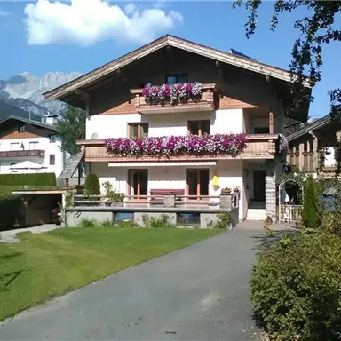 Ein charmantes Haus in den Alpen mit bunten Blumen auf dem Balkon. Der gepflegte Garten und die umliegenden Berge schaffen eine idyllische Atmosphäre.