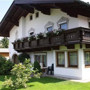 Ein schönes Haus im alpinen Stil mit einem Balkon, der mit Blumen geschmückt ist. Der gepflegte Garten und die sonnige Umgebung verleihen eine einladende Atmosphäre.