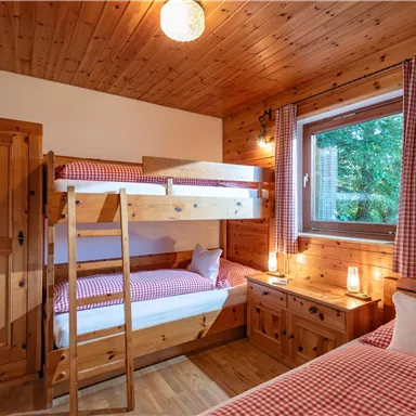Ein gemütliches Schlafzimmer aus Holz mit einem Etagenbett und einem Einzelbett. Das Fenster bietet einen Blick auf die Natur, und die Einrichtung wirkt einladend und warm.