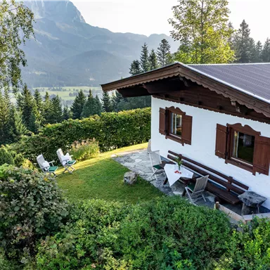 Ein idyllisches Ferienhaus in der Natur mit Blick auf die Berge. Im Garten stehen Liegestühle und ein Tisch für entspannte Momente im Freien.