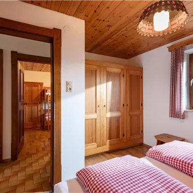 Ein gemütliches Schlafzimmer mit zwei Betten und Holzschränken. Die Fenster lassen viel Tageslicht herein und schaffen eine einladende Atmosphäre.