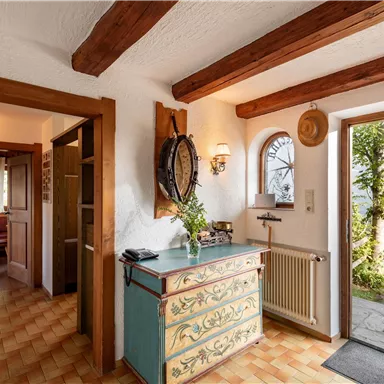 Ein einladender Eingangsbereich mit gemütlichem Holzinterieur und einem dekorativen Möbelstück. Durch das Fenster ist eine grüne Landschaft sichtbar.