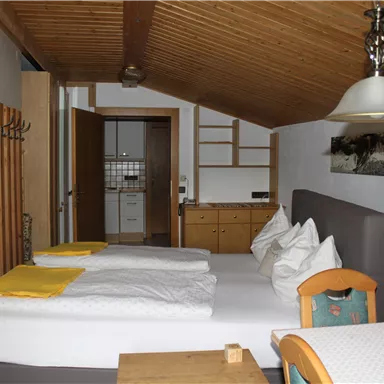 Ein gemütliches Schlafzimmer mit zwei Betten und Holzdecke. Der Raum ist mit einem Tisch und einem Fernseher ausgestattet.