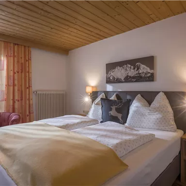 Ein gemütliches Schlafzimmer mit einem Doppelbett und warmen Farben. Große Fenster sorgen für viel Tageslicht und eine einladende Atmosphäre.