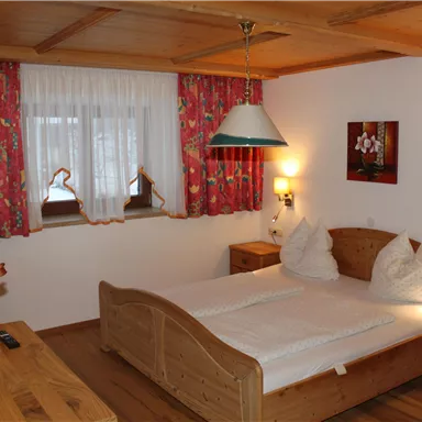 Ein gemütliches Schlafzimmer mit einem Doppelbett und Holzmöbeln. Die Wände sind mit bunten Vorhängen dekoriert, und es gibt eine kleine Sitzecke.