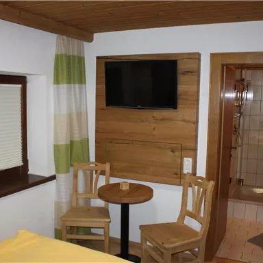 Ein gemütlicher Raum mit Holzdetails, zwei Stühlen und einem kleinen Tisch. An der Wand hängt ein Fernseher, und es gibt ein Badezimmer in der Nähe.