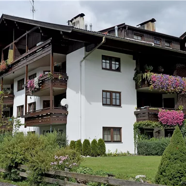 Ein charmantes Wohngebäude mit Blumenbalkonen und großem Garten. Die Umgebung ist grün und einladend.