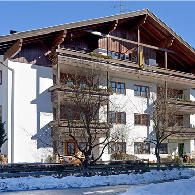 Ein modernes Mehrfamilienhaus mit Holzschnitt und großen Balkonen. Der Garten ist schneebedeckt und die Bäume sind kahl.