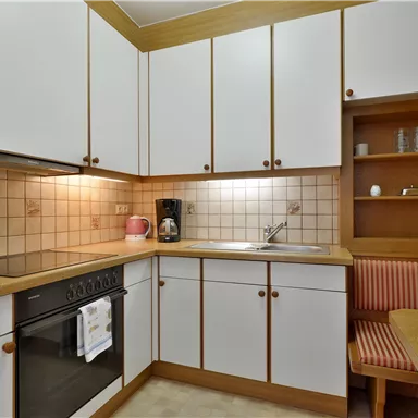 Eine moderne Küche mit weißen Schränken und einer gemütlichen Essecke. Die Ausstattung umfasst einen Herd, eine Spüle und eine Mikrowelle.