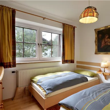 Ein gemütliches Schlafzimmer mit zwei Betten und warmen Farbtönen. Das Fenster lässt viel Licht herein und ein Kunstwerk schmückt die Wand.