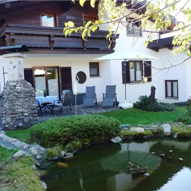 A cozy house with a small pond and a terrace. The surroundings are green and well-kept, ideal for relaxing.
