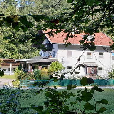 A beautiful house with a red roof, surrounded by trees and greenery. In the foreground, there are bushes and a colored fence line.