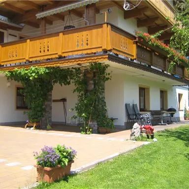 Ein gemütliches Haus mit einem Holz-Balkon und grünen Pflanzen. Der angrenzende Garten ist mit Rasen und Blumen ausgestattet.