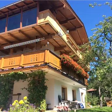 Ein charmantes Haus mit einem Holzbalcony und blühenden Pflanzen. Der klare Himmel und die grüne Umgebung schaffen eine einladende Atmosphäre.