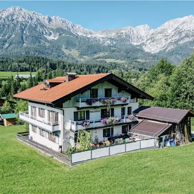 Ein schönes Haus in einer grünen Landschaft mit Blick auf die Berge. Der Himmel ist klar und die Umgebung ist ruhig und einladend.