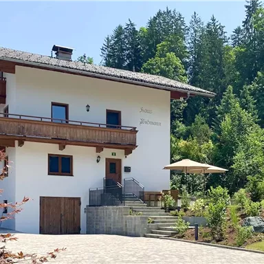Ein schönes Haus mit zwei Etagen, umgeben von Bäumen und einem gepflegten Garten. Der Himmel ist klar und die Umgebung ist grün und einladend.