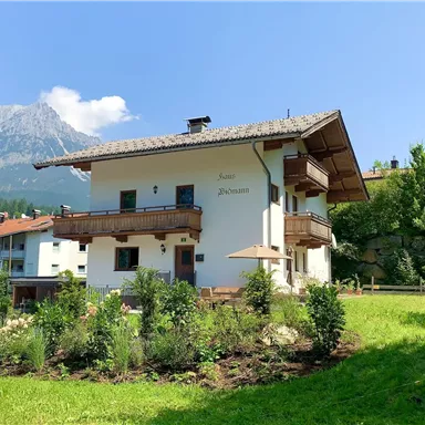 Ein charmantes Haus in den Alpen, umgeben von üppigem Grün und Bergen. Der klare Himmel verleiht der Szene eine friedliche Atmosphäre.