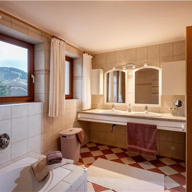 Ein modernes Badezimmer mit zwei Waschbecken und großen Spiegeln. Helle Fenster sorgen für viel Tageslicht und eine angenehme Atmosphäre.