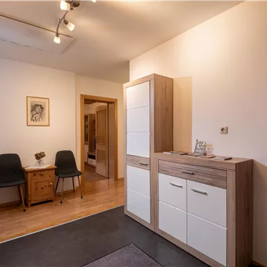 Ein moderner Flur mit Holzboden und ausreichend Stauraum. Zu sehen sind eine Kommode, Stühle und ein schönes Wandbild.