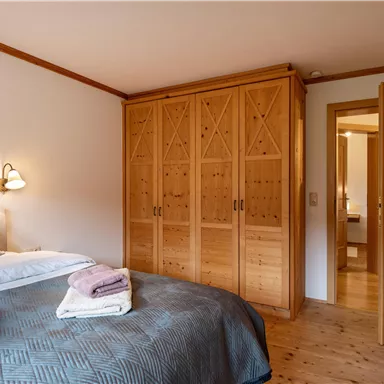 Ein gemütliches Schlafzimmer mit einem großen Boxspringbett und einem Holzschrank. Das Zimmer hat eine warme, einladende Atmosphäre.