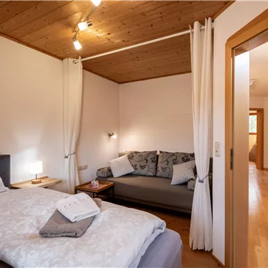 Ein gemütliches Schlafzimmer mit einem Doppelbett und einem Sofa. Der Raum ist hell und modern eingerichtet, mit Holzverkleidungen und warmem Licht.