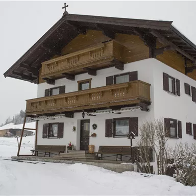 Ein wunderschönes zweigeschossiges Haus im alpinen Stil, umgeben von Schnee. Die Balkone und Fenster verleihen dem Gebäude einen charmanten Charakter.