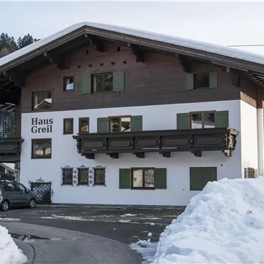 A cozy house in alpine style, surrounded by snow. The windows are green and the roof is overhanging.